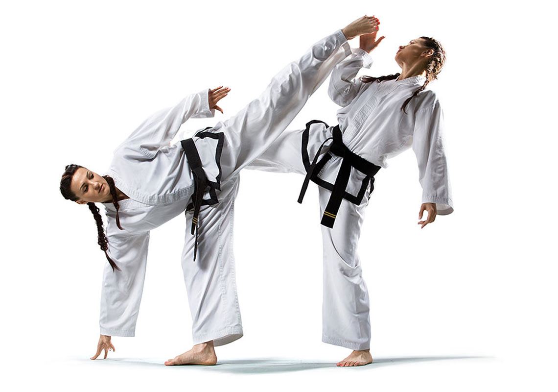 Zwei Frauen in Karatekleidung kämpfen vor weißem Hintergrund.