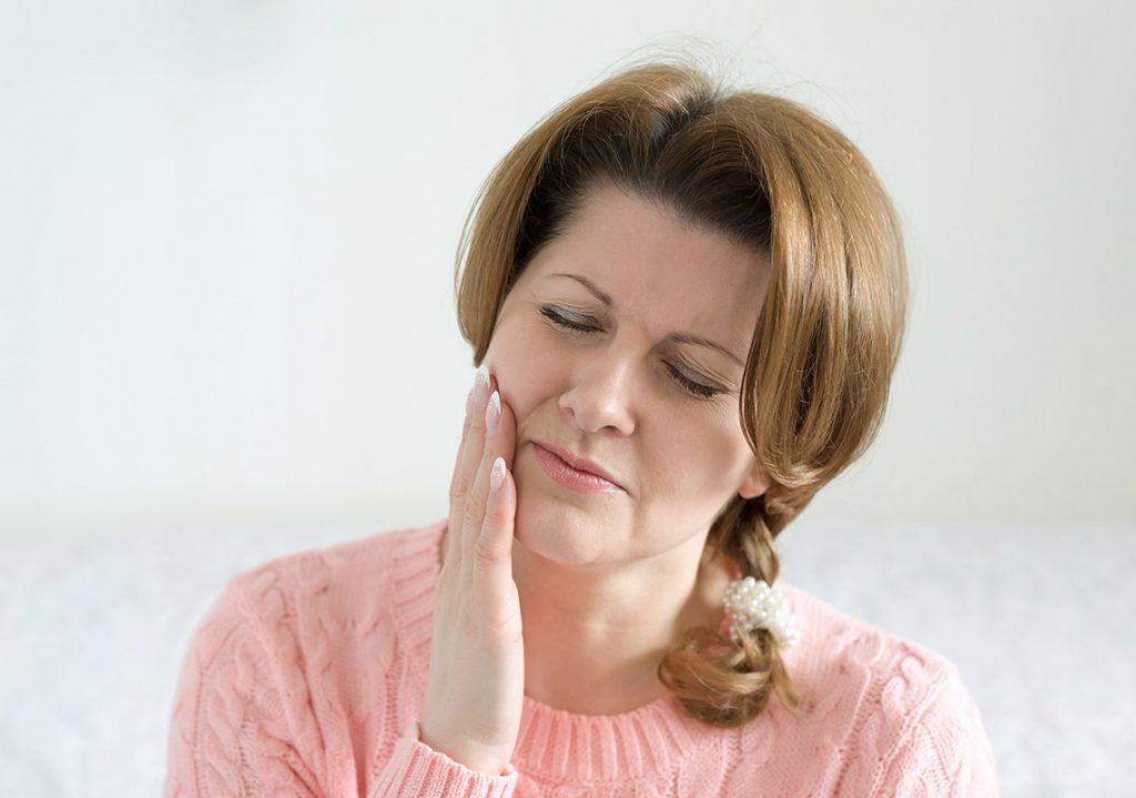 Eine Frau mit Zahnspangenschmerzen hält sich die Hand an die rechte Wange.