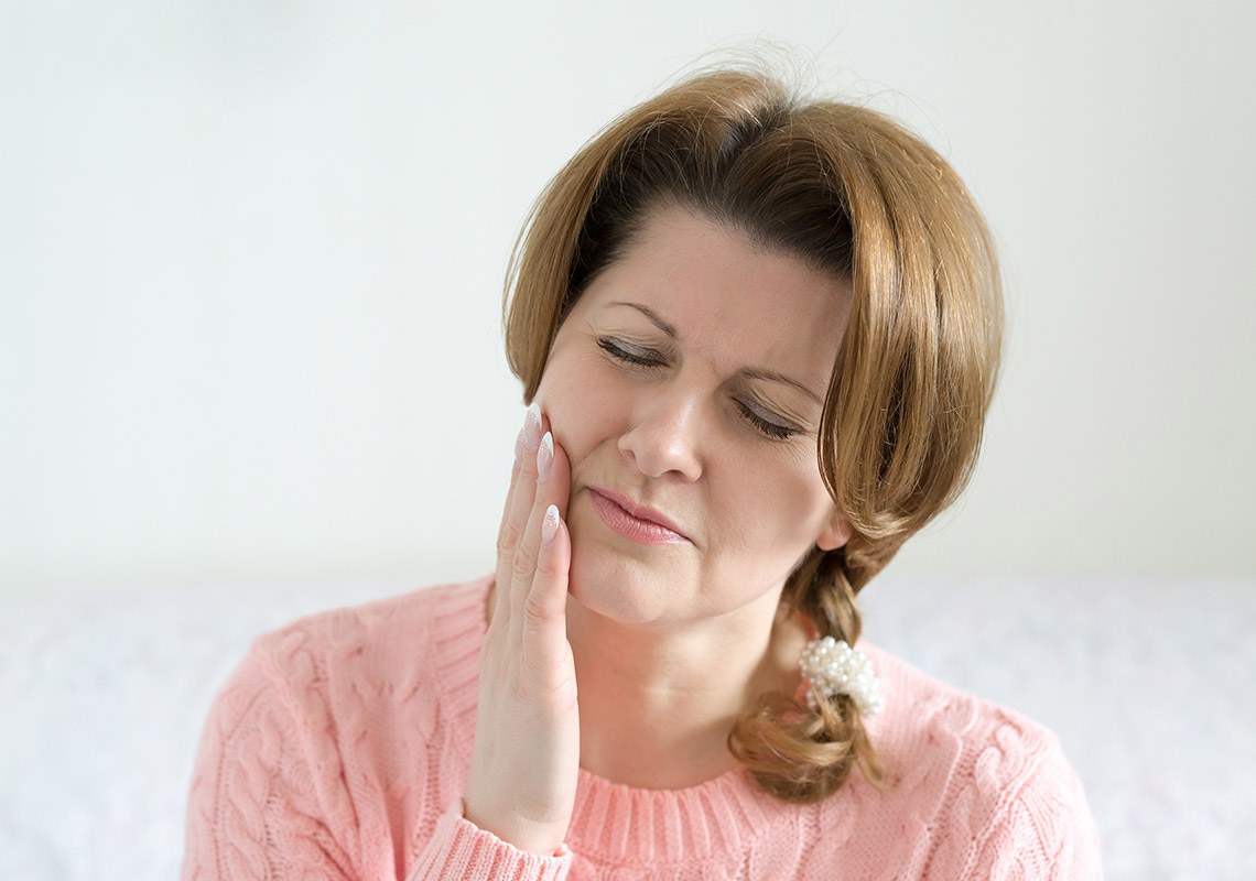 Eine Frau mit Zahnspangenschmerzen hält sich die Hand an die rechte Wange.